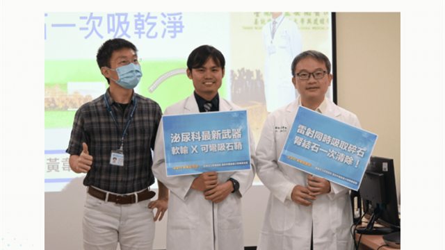 記者會現場三人並排合影，中間與右側兩位醫師手上各拿一塊看板，分別寫著「泌尿科最新武器 軟輸Ｘ可彎吸石鞘」與「雷射同時吸取碎石 腎結石一次清除」