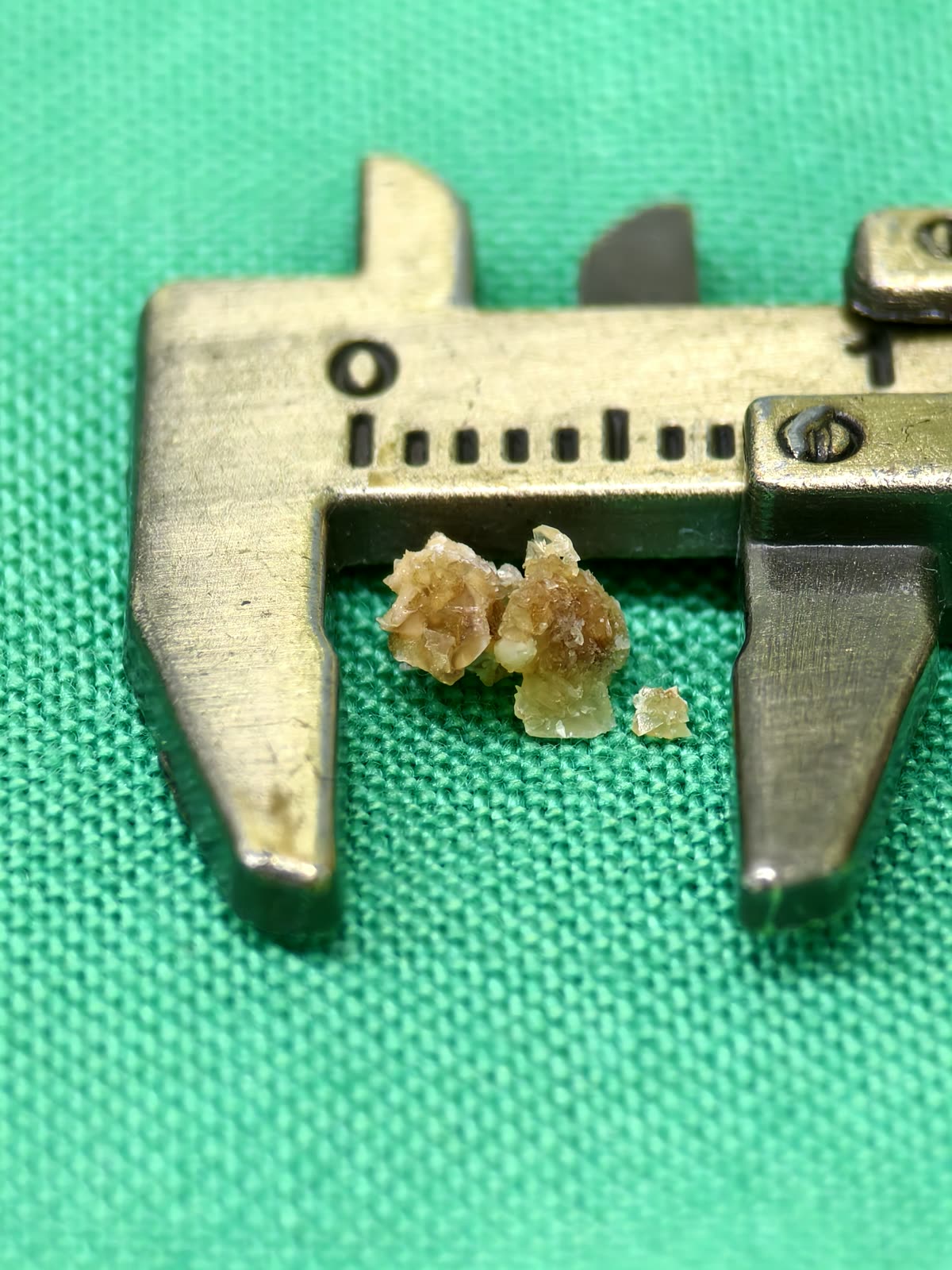 卡尺內幾顆淡琥珀色、半透明的片狀結晶碎塊
